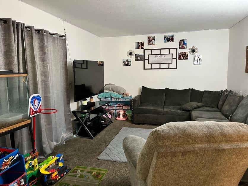 A living room features a dark sectional sofa, a television on a stand, and wall decor — 5885 DAHLIA DRIVE UNIT 24, ORLANDO, FL