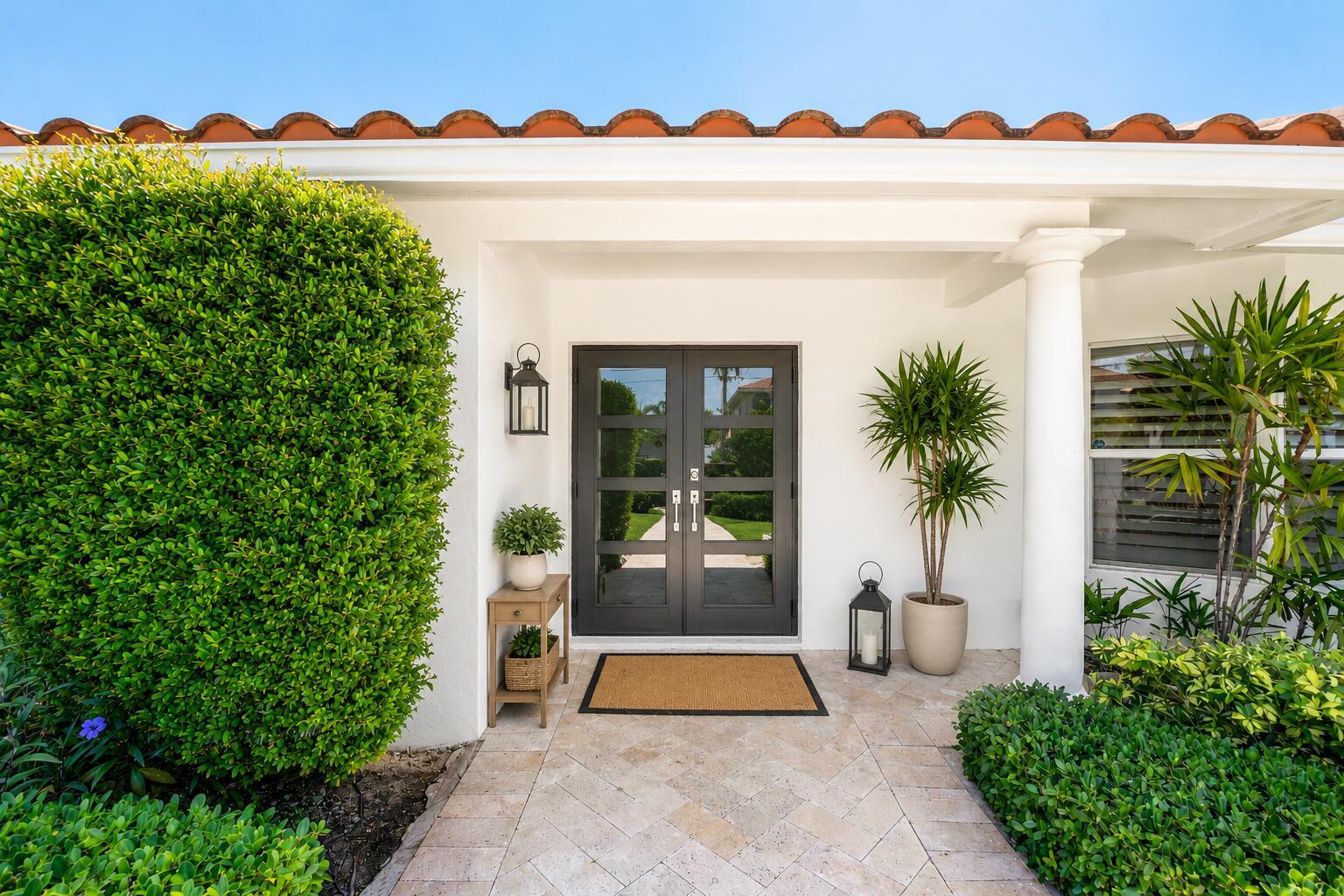 A white house exterior features a dark double door, a tiled entryway, and lush landscaping — 4230 NE 24th Avenue, Lighthouse Point FL 33064, LIGHTHOUSE POINT, FL