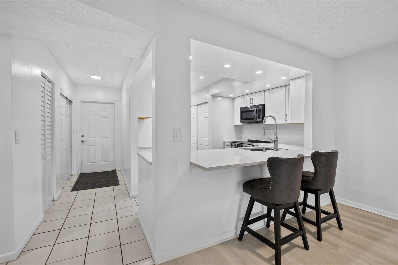 A kitchen with white cabinets and a breakfast bar overlooks a tiled entryway — 1700 NW 80th Avenue # 104, Margate FL 33063, MARGATE, FL