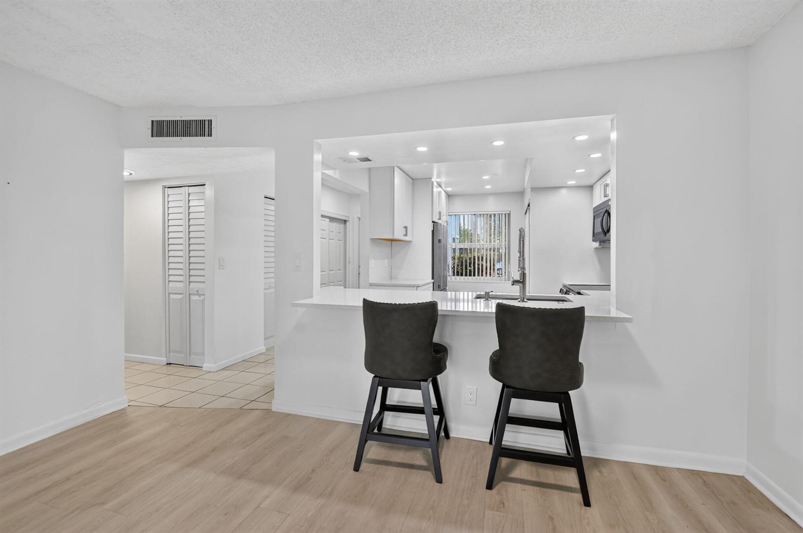 A kitchen pass-through window with a breakfast bar and two stools overlooks a living area — 1700 NW 80th Avenue # 104, Margate FL 33063, MARGATE, FL