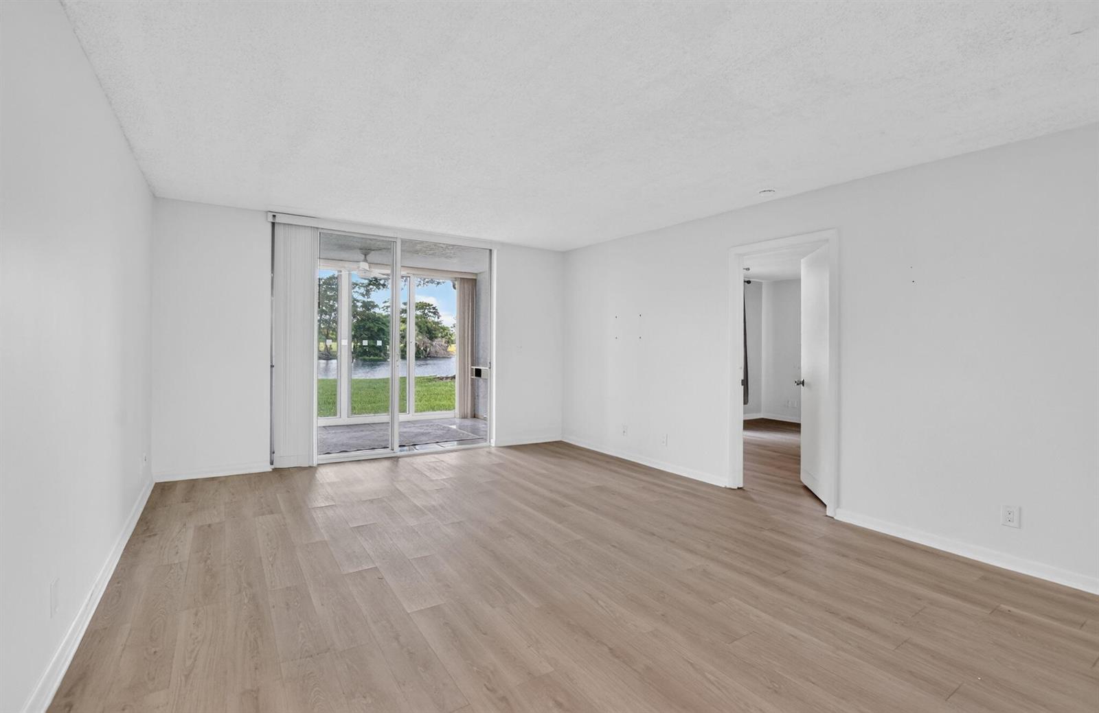 An empty room with light wood-look flooring, white walls, and a sliding glass door — 1700 NW 80th Avenue # 104, Margate FL 33063, MARGATE, FL