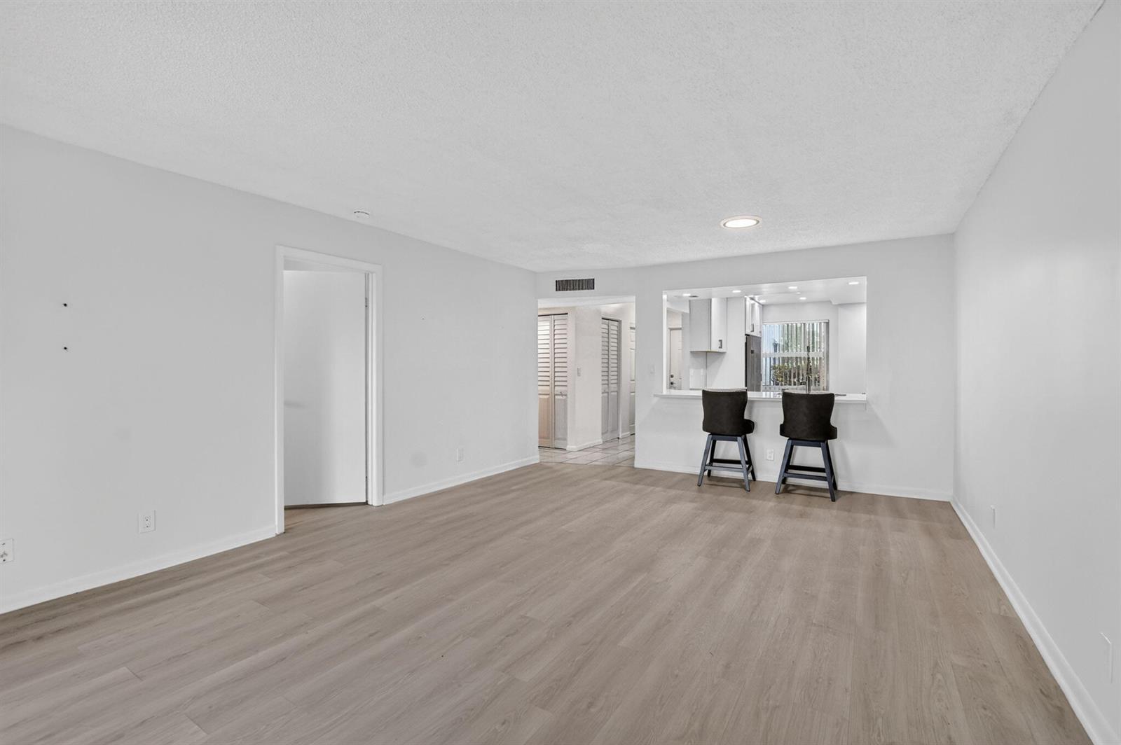 An empty living room with light wood-look flooring, white walls, and a kitchen pass-through window — 1700 NW 80th Avenue # 104, Margate FL 33063, MARGATE, FL