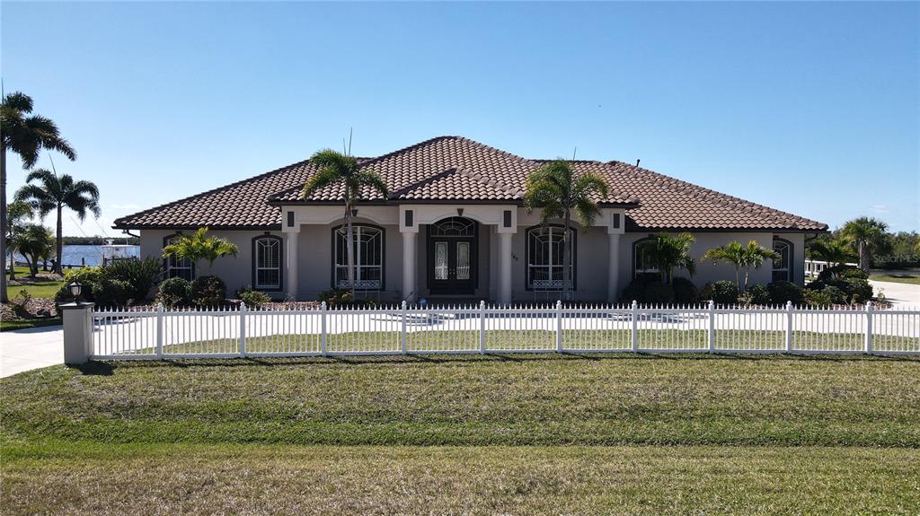 A single-story house with a tiled roof and white fence sits near the water — 17449 OHARA DRIVE, PORT CHARLOTTE, FL