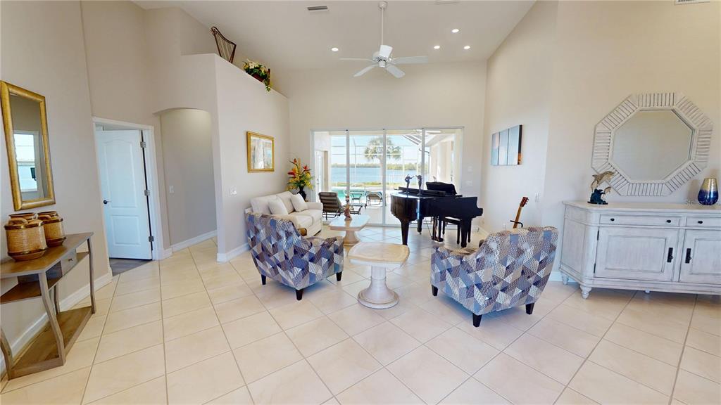 A living room features a grand piano, patterned armchairs, and a view of a pool — 17449 OHARA DRIVE, PORT CHARLOTTE, FL