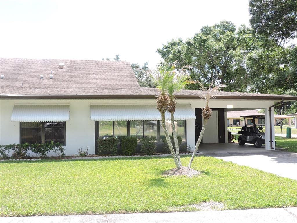 A white house with a shingled roof, white awnings, and a carport with a golf cart — 281 GENESIS POINTE DRIVE UNIT 8-3, LAKE WALES, FL