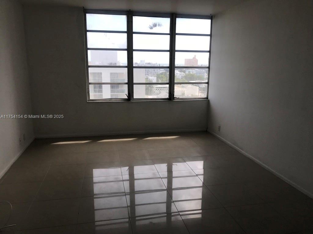 An empty room features light-colored tile flooring and a large window with a city view — 1000 West Ave # 908, Miami Beach FL 33139, MIAMI BEACH, FL