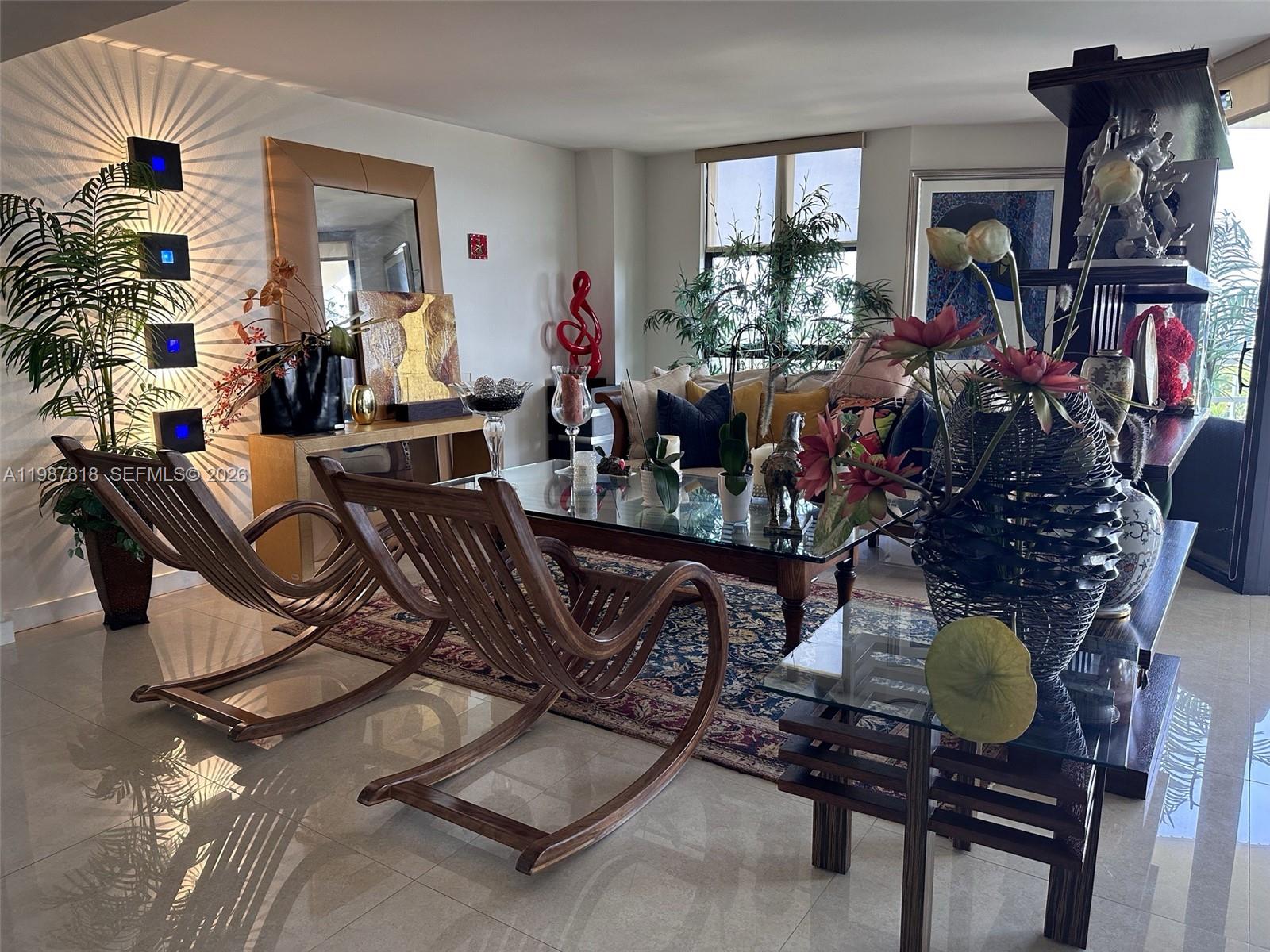 A living room features two wooden rocking chairs, a glass coffee table, and decorative lighting — 1000 Quayside Ter # 1101, Miami FL 33138, MIAMI, FL