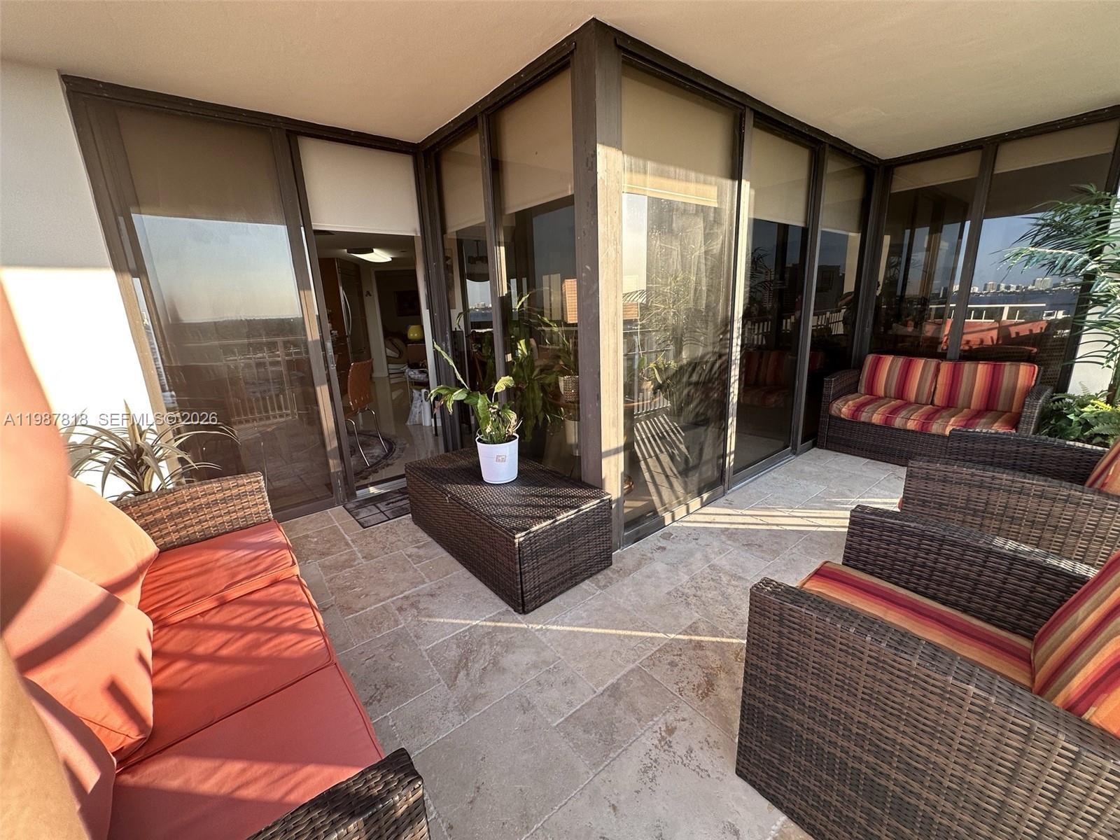 A furnished balcony features wicker seating, stone tile flooring, and floor-to-ceiling glass walls — 1000 Quayside Ter # 1101, Miami FL 33138, MIAMI, FL