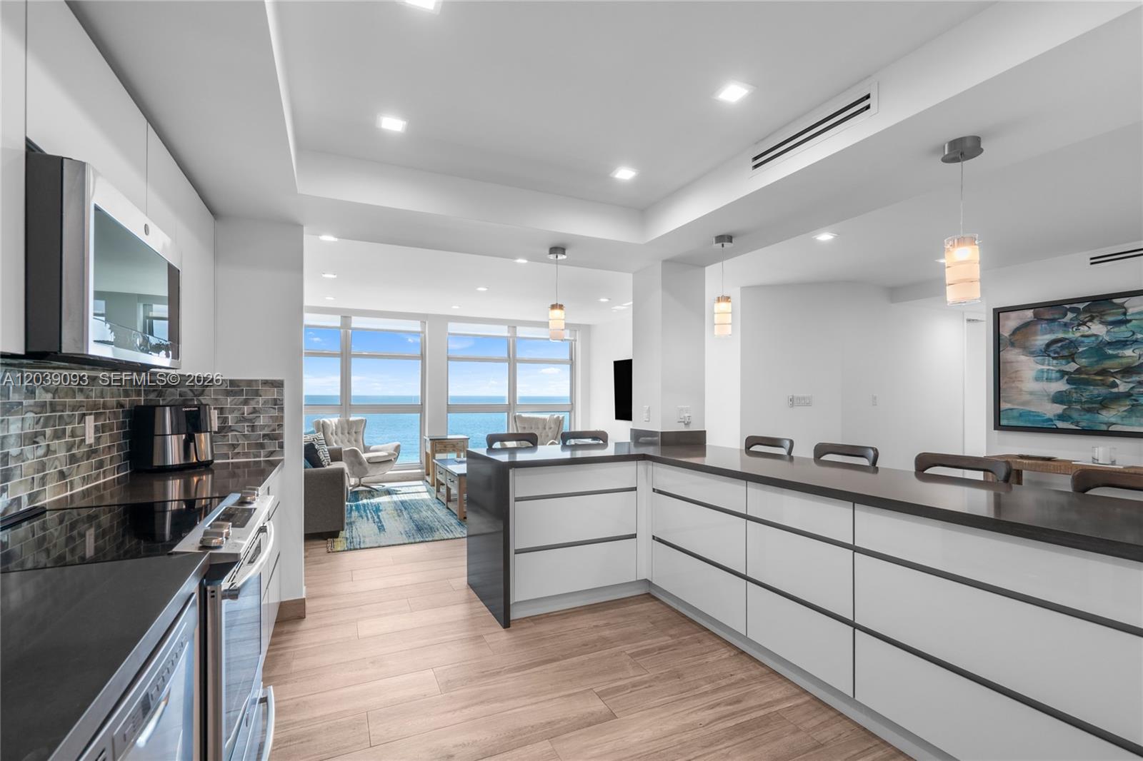A modern kitchen with white cabinets and dark countertops overlooks a living area with ocean views — 5055 Collins Ave # 10H, Miami Beach FL 33140, MIAMI BEACH, FL