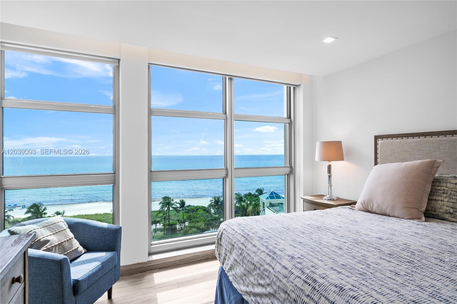A bedroom features a bed, a blue armchair, and large windows overlooking the ocean — 5055 Collins Ave # 10H, Miami Beach FL 33140, MIAMI BEACH, FL