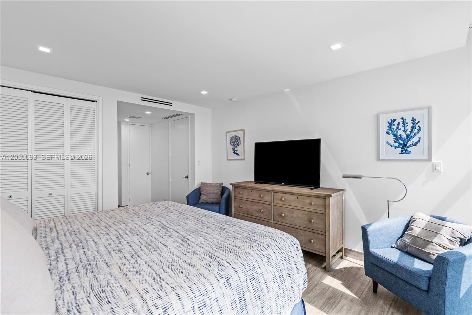 A bedroom features a bed, a wooden dresser with a television, and two blue armchairs — 5055 Collins Ave # 10H, Miami Beach FL 33140, MIAMI BEACH, FL