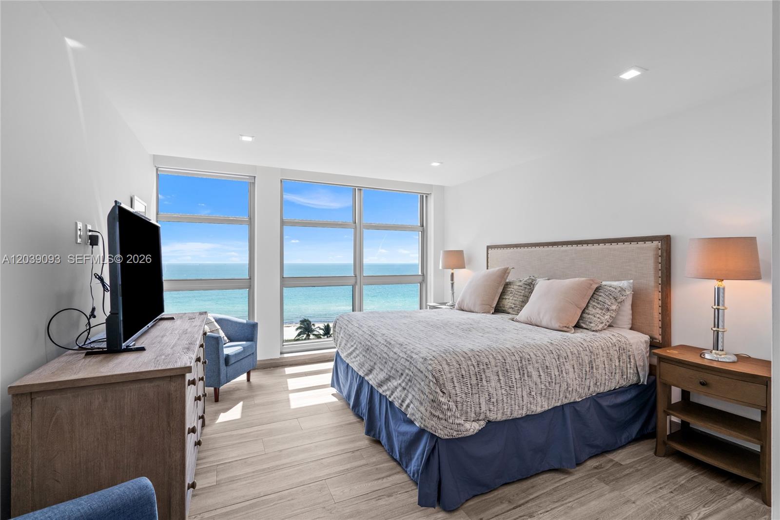 A bedroom features a king bed, wooden furniture, and floor-to-ceiling windows overlooking the ocean — 5055 Collins Ave # 10H, Miami Beach FL 33140, MIAMI BEACH, FL
