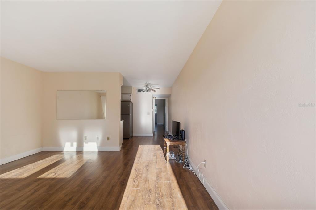 A living room with wood-look flooring, beige walls, a mirror, and an adjacent kitchen area — 4565 DUHME ROAD UNIT 203, ST PETERSBURG, FL