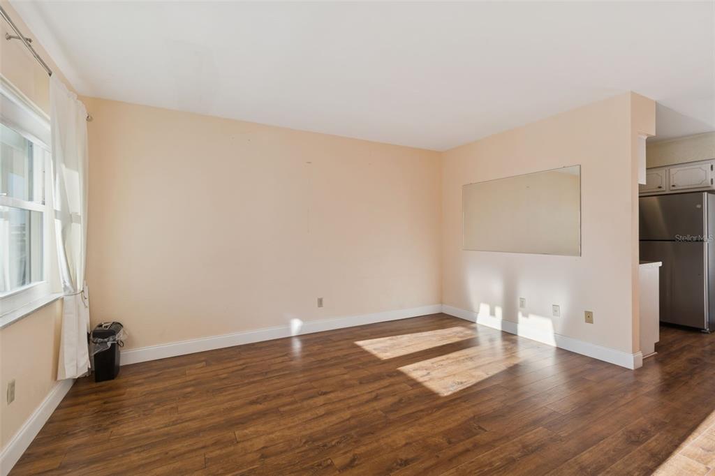 An empty room with wood-look flooring, beige walls, a large wall mirror, and a window — 4565 DUHME ROAD UNIT 203, ST PETERSBURG, FL