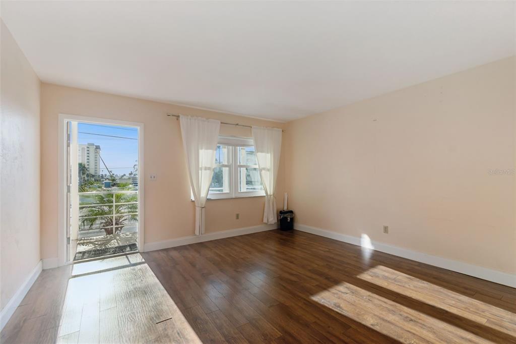 An empty room features wood-look flooring, light-colored walls, a window with curtains, and a door — 4565 DUHME ROAD UNIT 203, ST PETERSBURG, FL