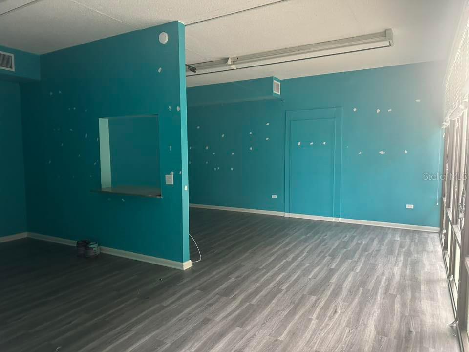 An interior room with teal walls, gray wood-look flooring, and a pass-through window — 2595 TAMIAMI TRAIL, PORT CHARLOTTE, FL