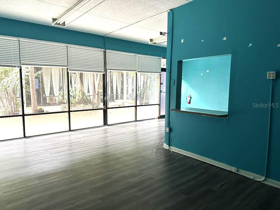 An empty room features teal walls, large windows with blinds, and dark wood-look flooring — 2595 TAMIAMI TRAIL, PORT CHARLOTTE, FL