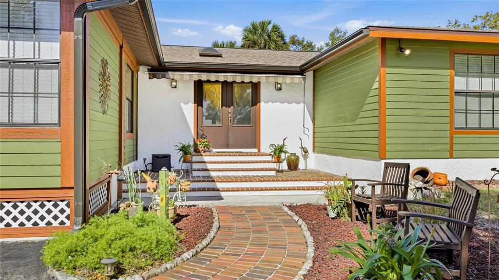A brick walkway leads to the front entrance of a house with green siding — 906 TROPICAL DRIVE, BRADENTON, FL