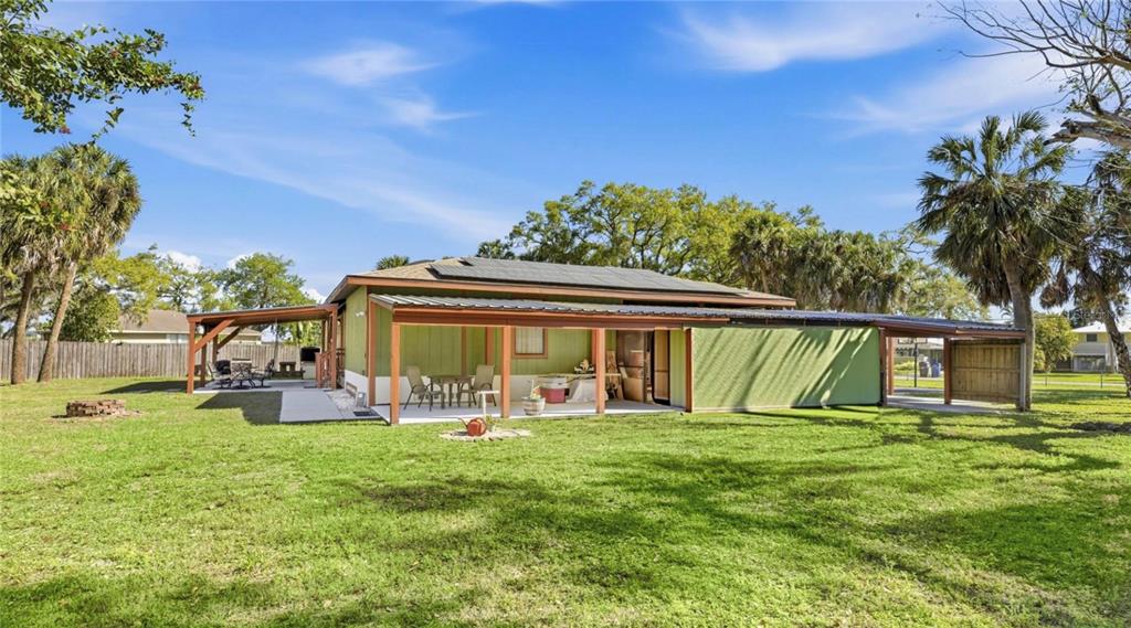 The exterior of a single-story house features a covered patio, metal roof, and solar panels — 906 TROPICAL DRIVE, BRADENTON, FL