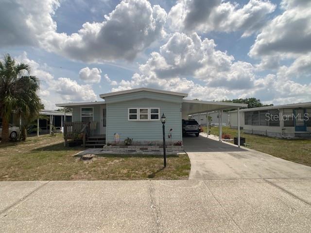 A light blue manufactured home with a front porch, attached carport, and concrete driveway — 1710 7TH STREET SW UNIT 24, RUSKIN, FL