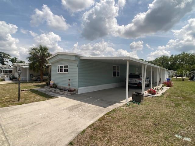 A light blue mobile home features a concrete driveway, a carport, and a small garden bed — 1710 7TH STREET SW UNIT 24, RUSKIN, FL