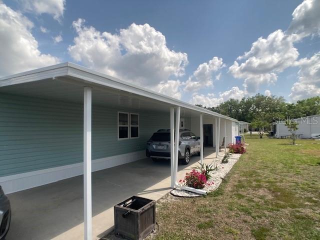 A light blue mobile home features a long covered carport and a small landscaped garden — 1710 7TH STREET SW UNIT 24, RUSKIN, FL