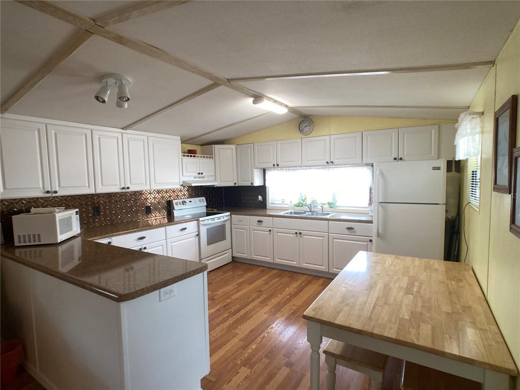 A kitchen with white cabinets, brown countertops, wood-look flooring, and a wooden dining table — 1710 7TH STREET SW UNIT 24, RUSKIN, FL