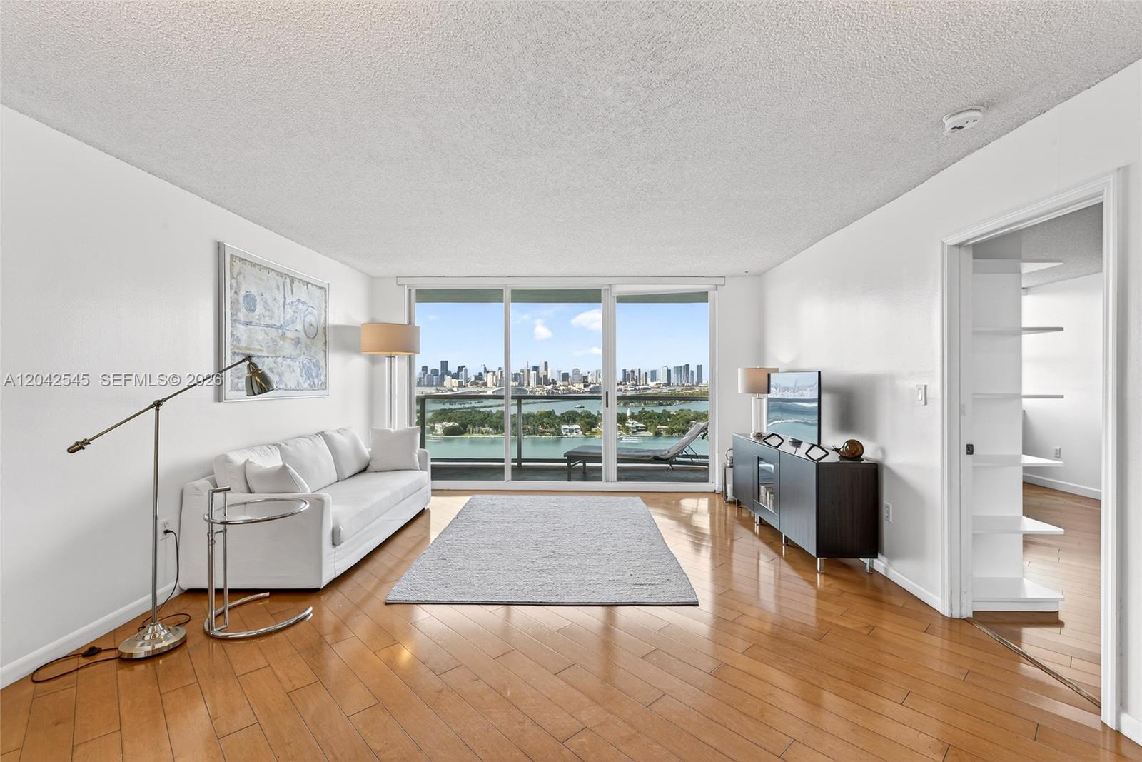 A living room with hardwood floors, a white sofa, and a balcony overlooking a city — MIAMI BEACH, FL