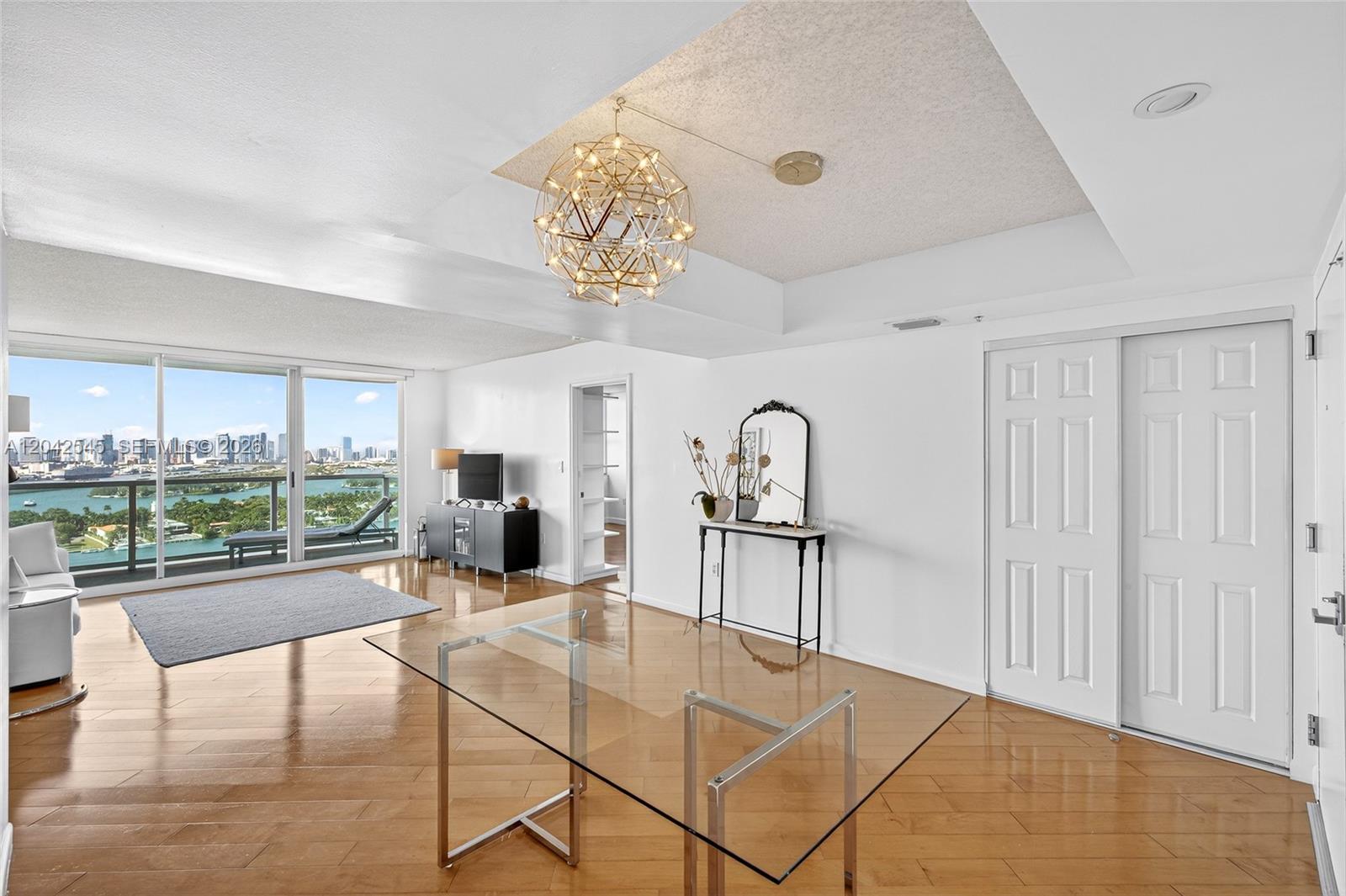 A bright living and dining area features hardwood floors, a modern chandelier, and balcony views — MIAMI BEACH, FL