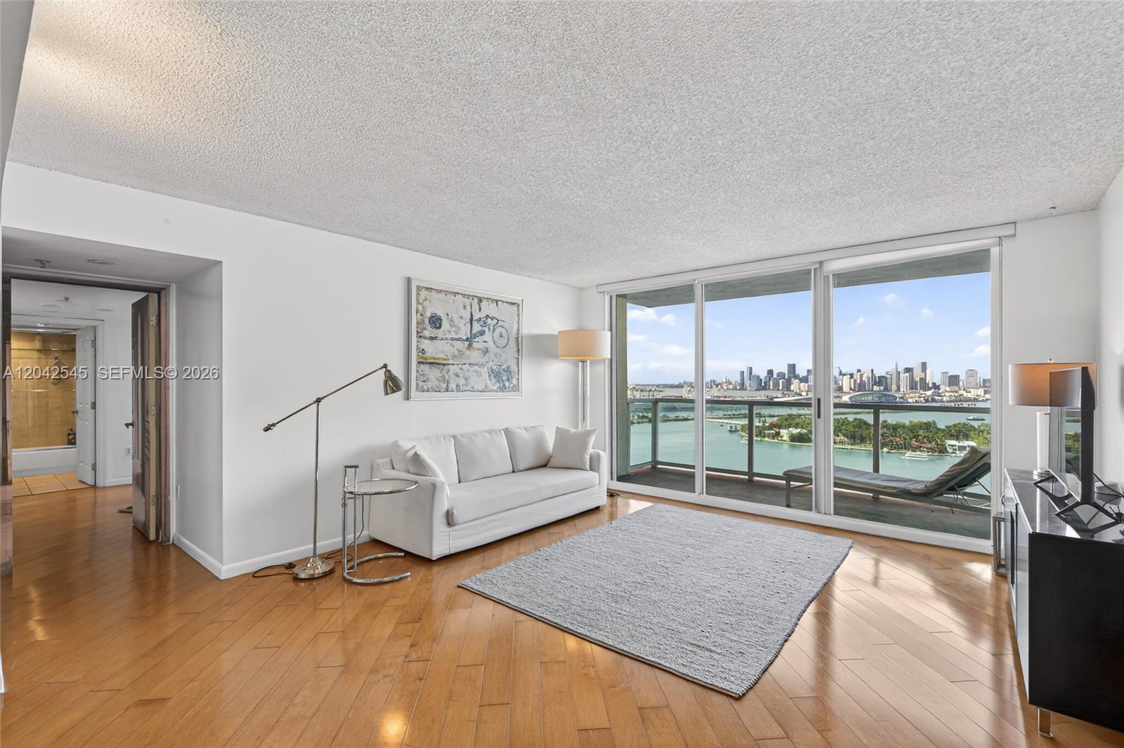 A living room with hardwood floors, a white sofa, and a balcony overlooking a city skyline — MIAMI BEACH, FL