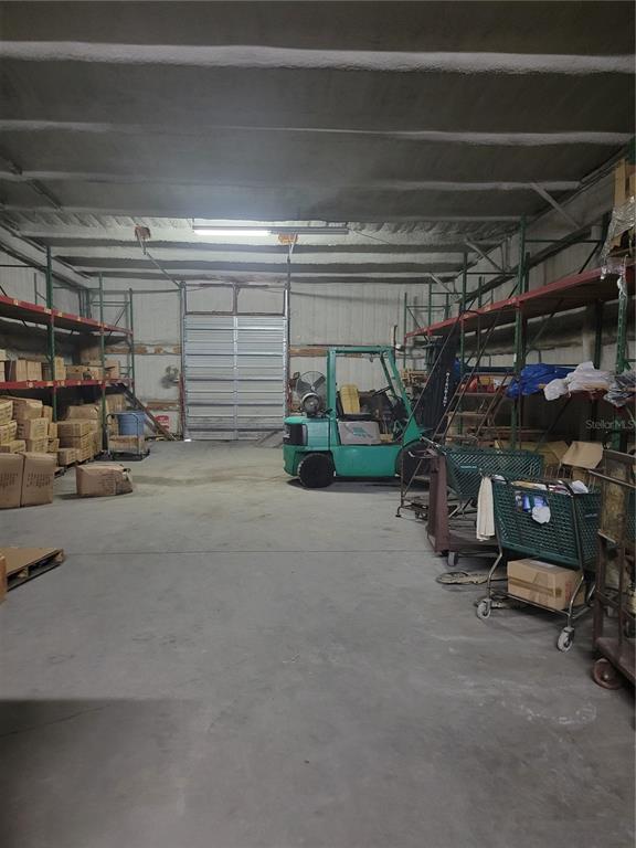 A warehouse interior features concrete floors, metal shelving units, and a green forklift — 2437 E CR 478 AVENUE, WEBSTER, FL