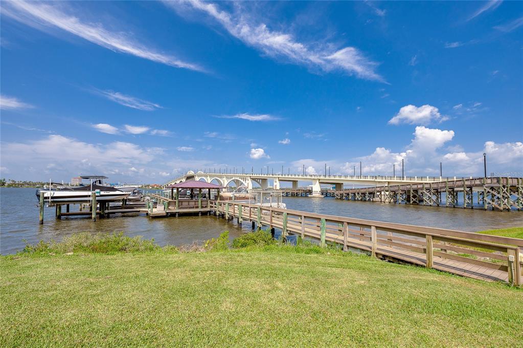 A wooden pier and boat dock extend into a river toward a large concrete bridge — 100 SILVER BEACH AVENUE UNIT 308, DAYTONA BEACH, FL