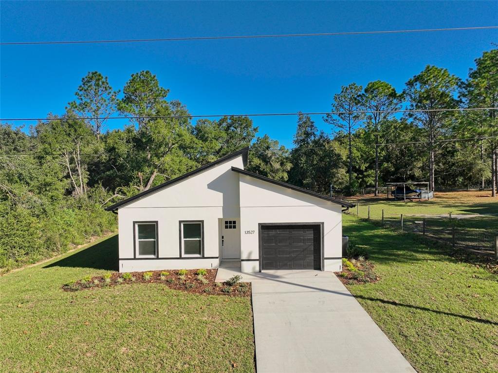 A modern, white, single-story house with a black roof and garage sits on a lawn — 13527 SW 100TH LANE, DUNNELLON, FL