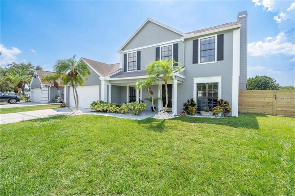 A two-story gray house with a white garage, palm trees, and a wooden fence — 16208 PEBBLEBROOK DRIVE, TAMPA, FL