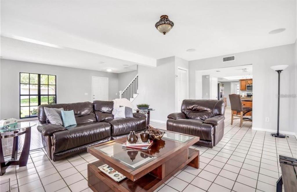 A living room with white tile floors, brown leather furniture, and a wooden coffee table — 16208 PEBBLEBROOK DRIVE, TAMPA, FL