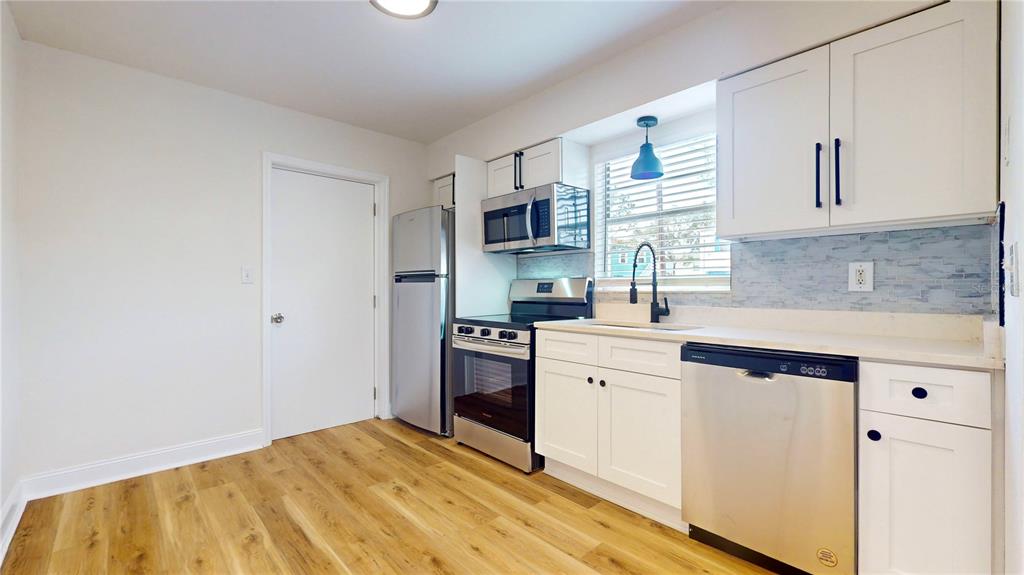 A kitchen features white cabinets, stainless steel appliances, and light wood-look flooring — 6710 S JUANITA STREET, TAMPA, FL