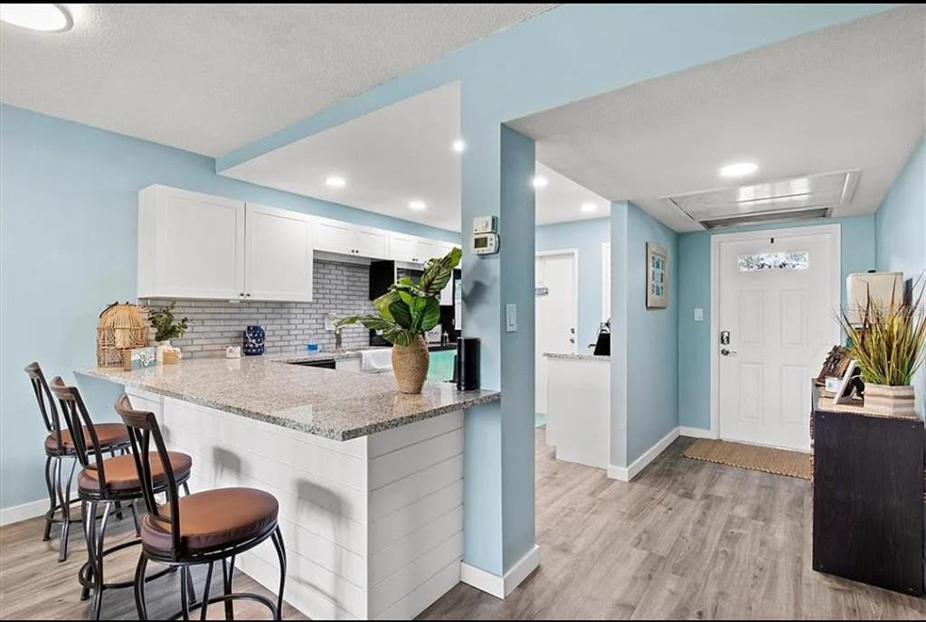 A kitchen with a granite breakfast bar and white cabinets opens to an entryway — 7461 W COUNTRY CLUB DRIVE N UNIT 108, SARASOTA, FL