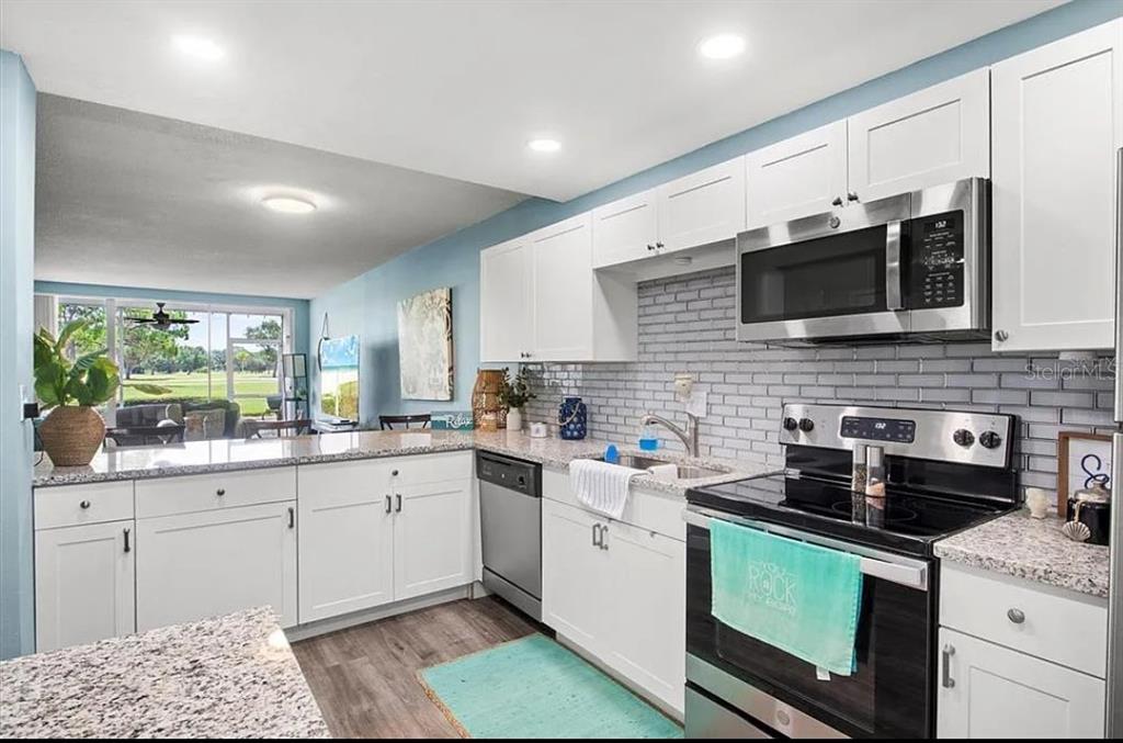 A kitchen with white cabinets, granite countertops, a gray brick backsplash, and stainless steel appliances — 7461 W COUNTRY CLUB DRIVE N UNIT 108, SARASOTA, FL