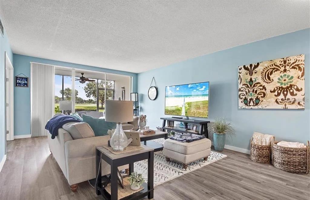 A living room features light blue walls, wood-look flooring, a sofa, and a television — 7461 W COUNTRY CLUB DRIVE N UNIT 108, SARASOTA, FL