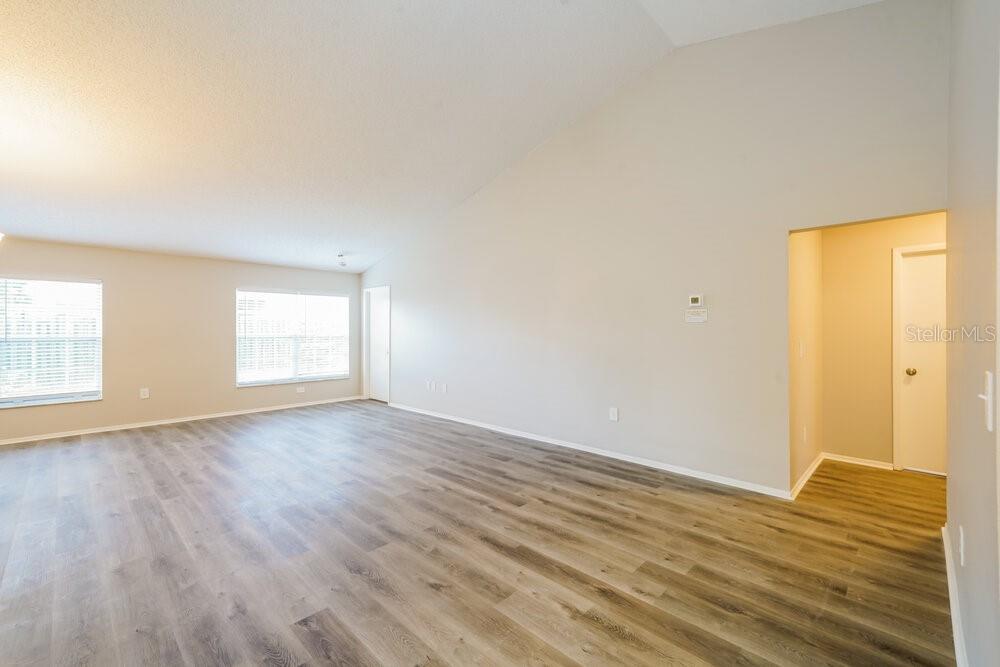 An empty living room features vaulted ceilings, light-colored walls, and wood-look vinyl plank flooring — 1434 LAKEHURST WAY, BRANDON, FL