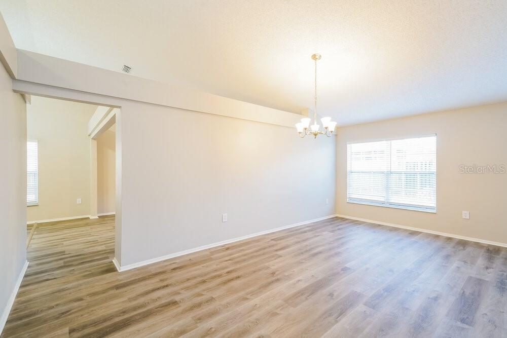 An empty dining room features light gray walls, wood-look flooring, and a hanging light fixture — 1434 LAKEHURST WAY, BRANDON, FL