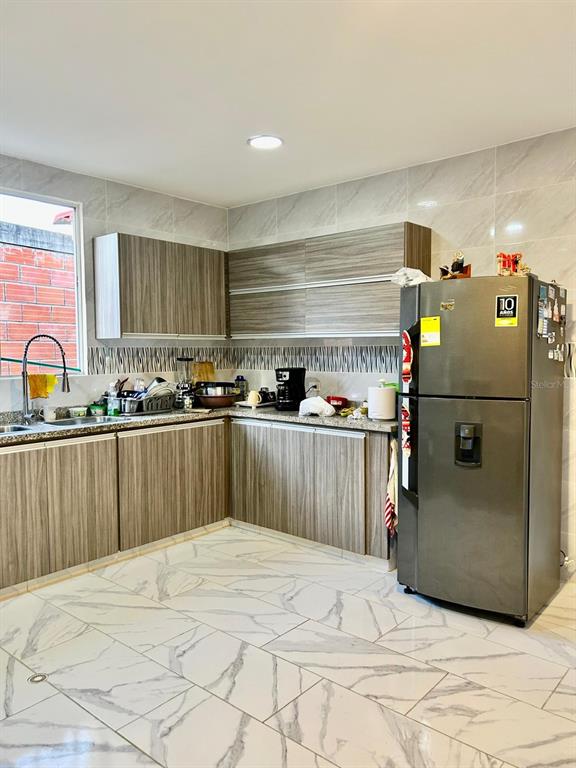 A kitchen features wood-grain cabinets, a stainless steel refrigerator, and white marble-patterned floor tiles — Cra 11 #7-72, SANTA VERONICA, ATLANTICO, OC
