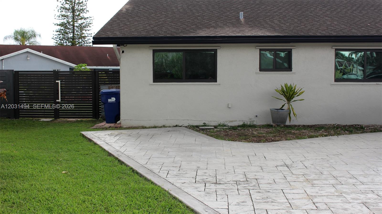 A paved patio area sits beside the exterior wall of a house with dark-framed windows — 14680 SW 107th Ter, Miami FL 33186, MIAMI, FL