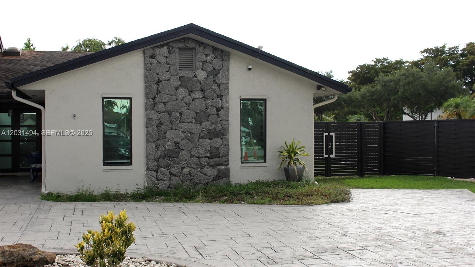 The exterior of a house features a stone accent wall, two windows, and a paved driveway — 14680 SW 107th Ter, Miami FL 33186, MIAMI, FL