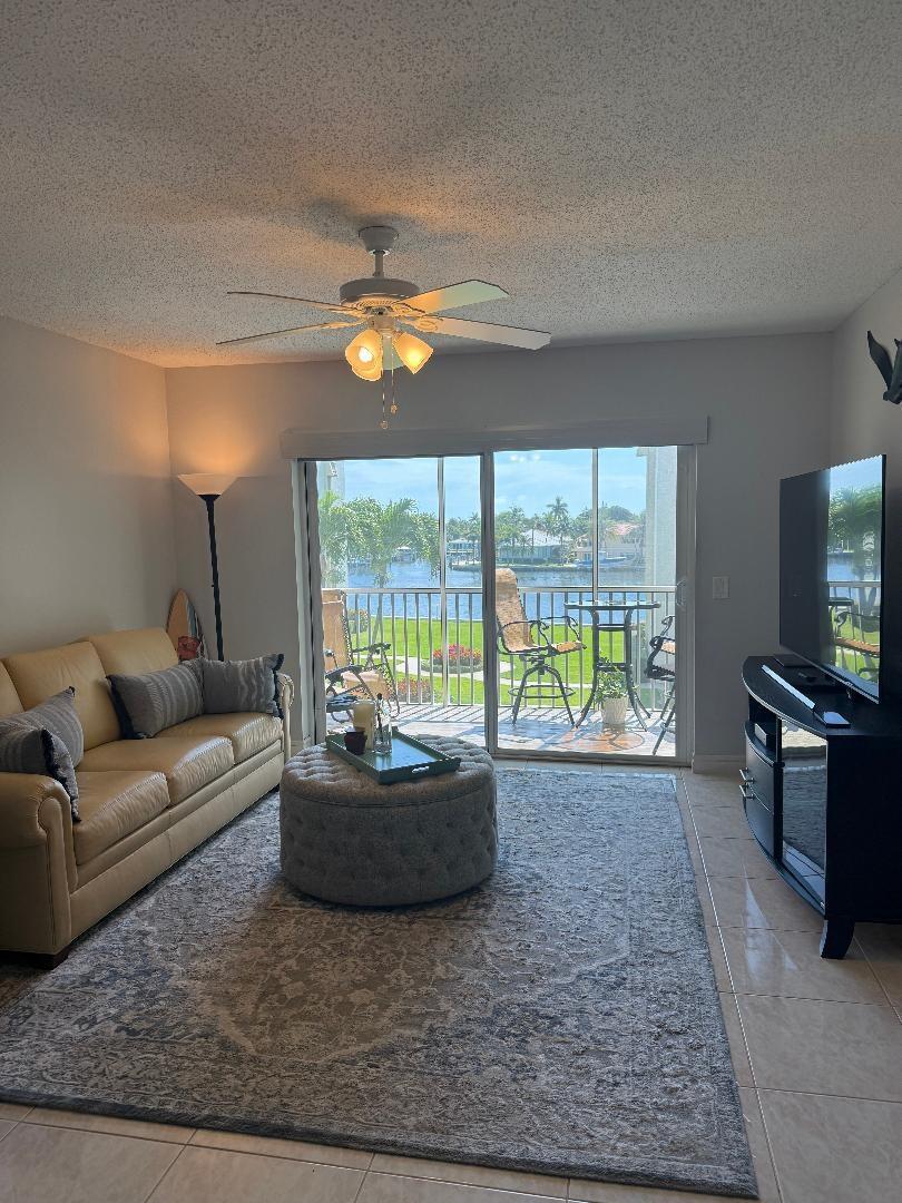 A living room with a tan sofa, round ottoman, and sliding glass doors overlooking a canal — 646 Snug Harbor Drive # H308, Boynton Beach FL 33435, BOYNTON BEACH, FL