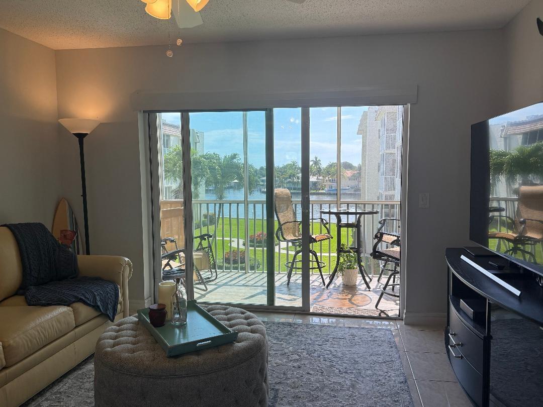 A living room with a beige sofa, tufted ottoman, and sliding glass doors to a balcony — 646 Snug Harbor Drive # H308, Boynton Beach FL 33435, BOYNTON BEACH, FL