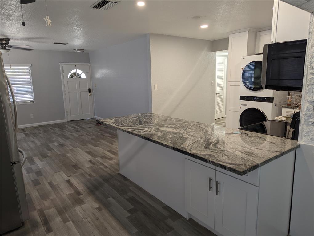 A kitchen island with granite countertops sits in an open-concept room with gray wood flooring — 206 N GUNLOCK AVENUE, TAMPA, FL