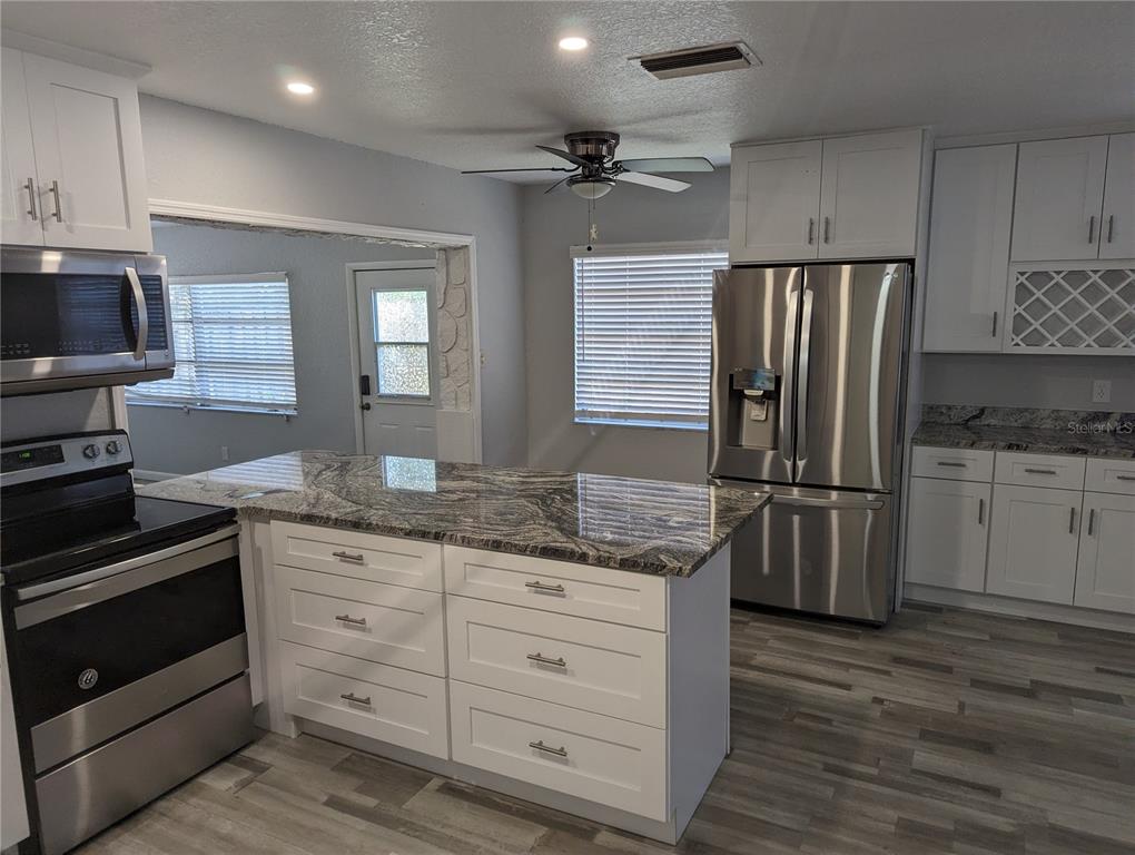 A kitchen features white cabinetry, granite countertops, a center island, and stainless steel appliances — 206 N GUNLOCK AVENUE, TAMPA, FL