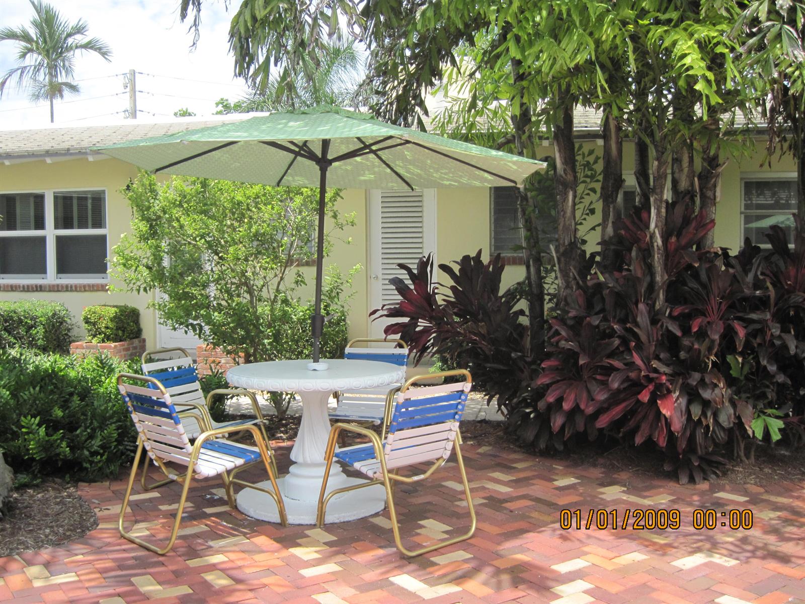 A patio with a round table, umbrella, and four chairs sits on a brick surface — 30 Andrews Avenue # 23c, Delray Beach FL 33483, DELRAY BEACH, FL