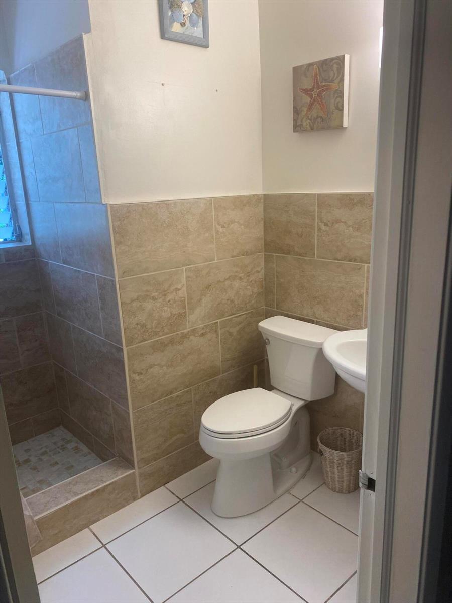 A small bathroom features a tiled walk-in shower, a white toilet, and a pedestal sink — 30 Andrews Avenue # 23c, Delray Beach FL 33483, DELRAY BEACH, FL
